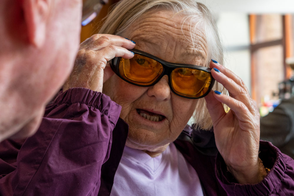 Group member wearing fitover sunglasses speaking to another client about assistive technology
